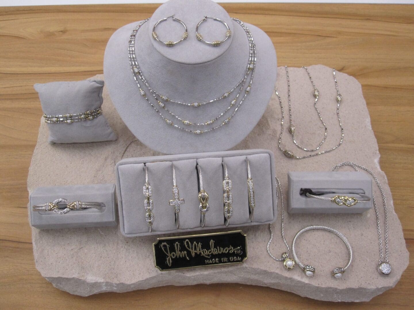 A display of silver jewelry including necklaces, earrings, rings, and bracelets, arranged around a hat on a textured surface.