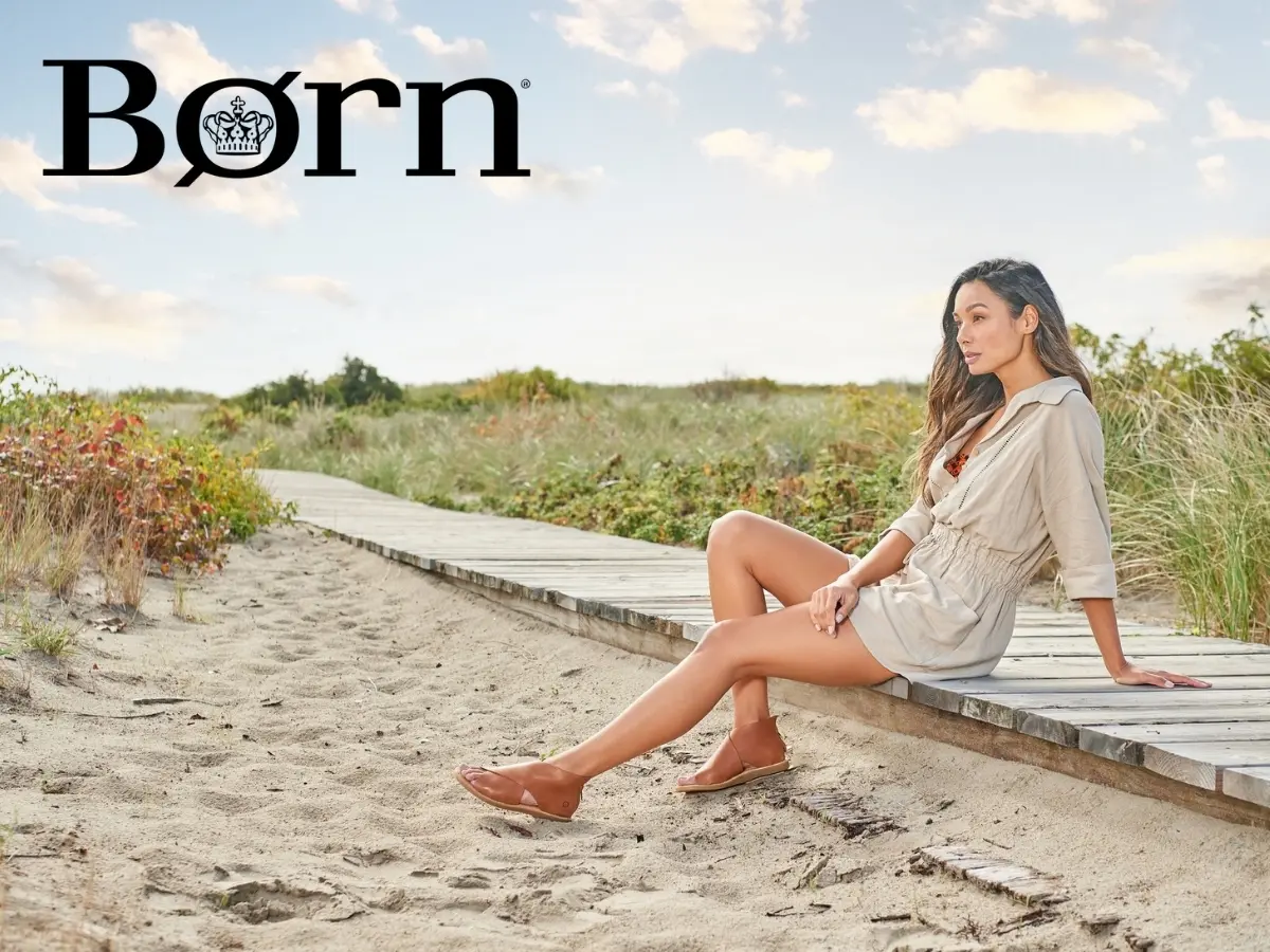 A woman sits on a wooden boardwalk by the beach, wearing casual summer attire and shoes from the born brand.