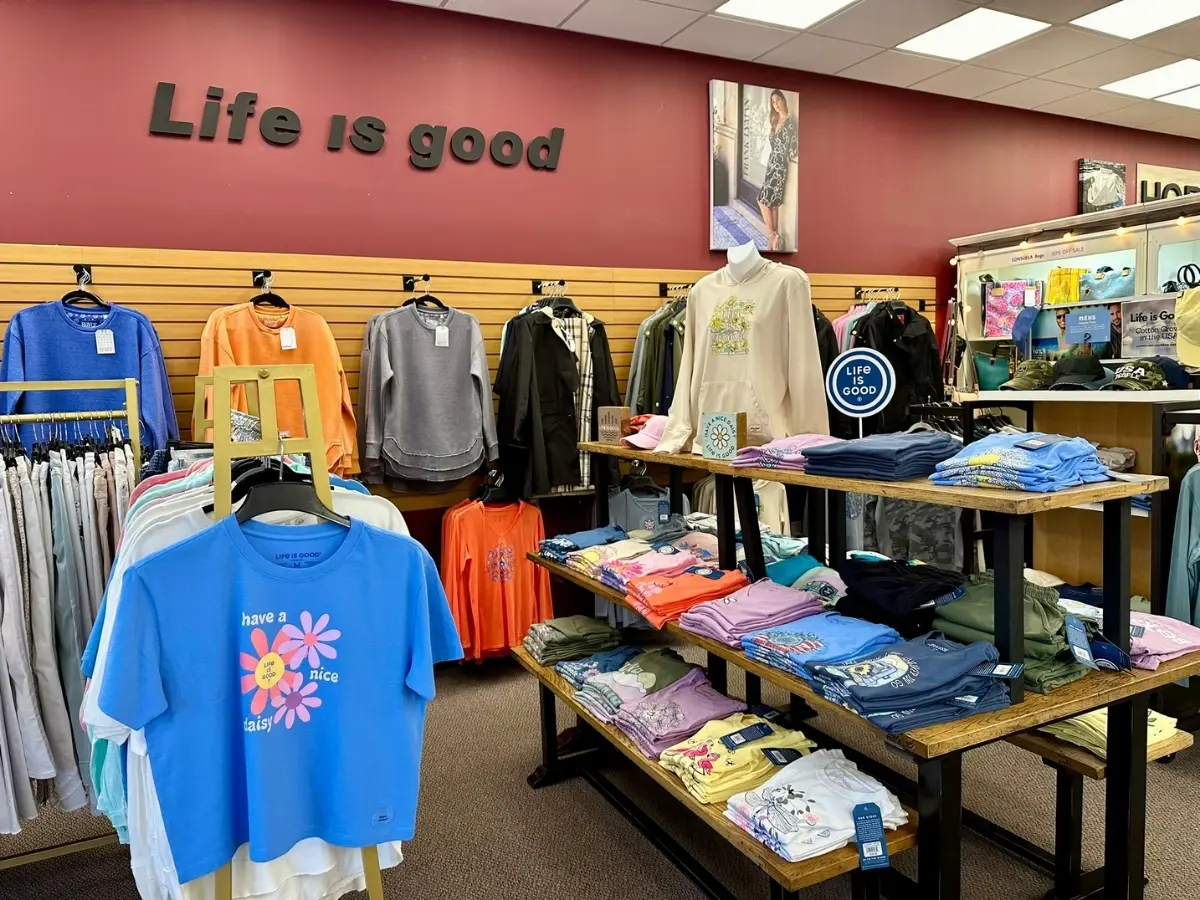 A well-organized clothing store with a "life is good" sign displayed above a variety of colorful apparel.