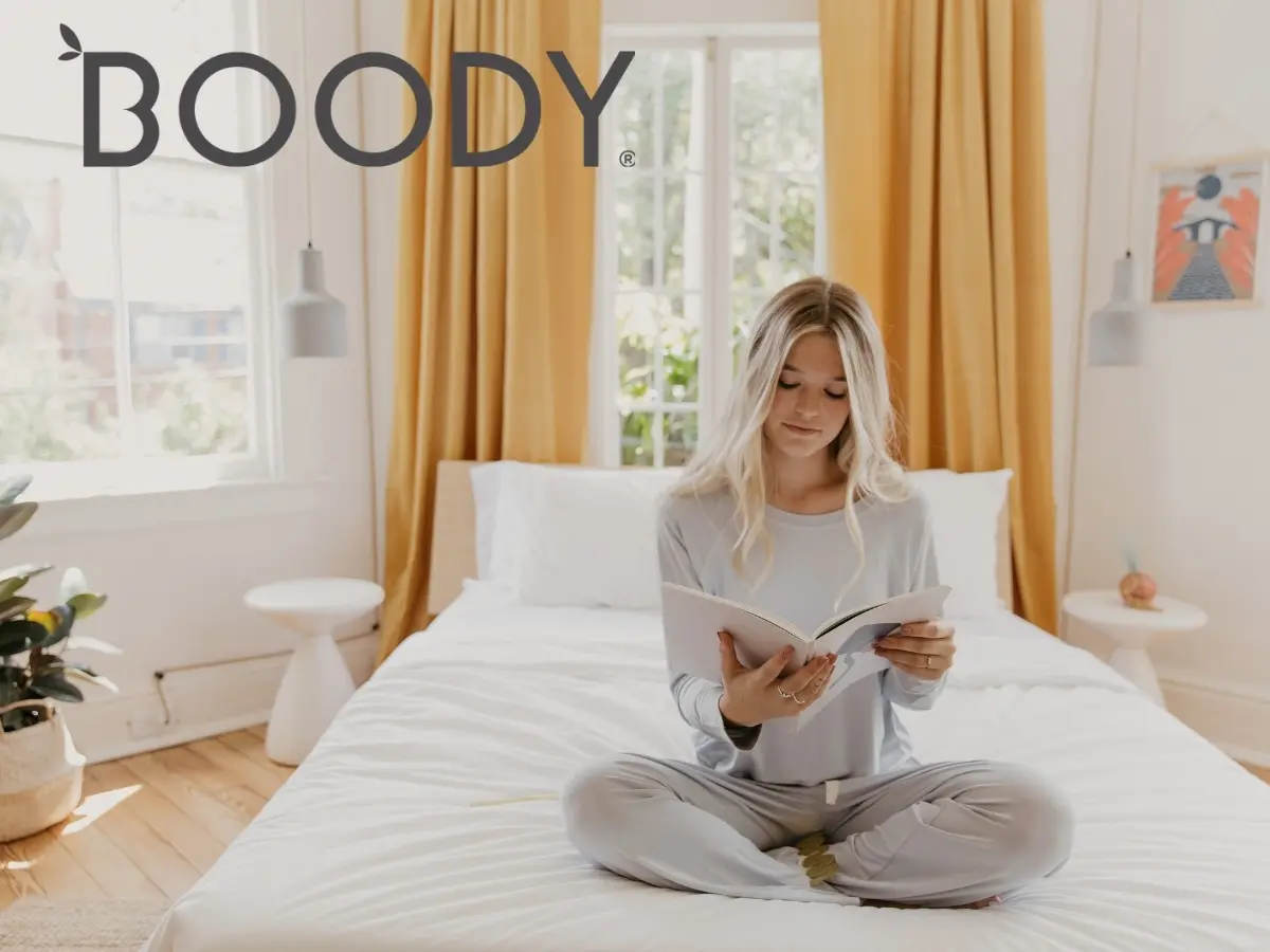 Woman reading a book on a bed in a bright, cozy room.