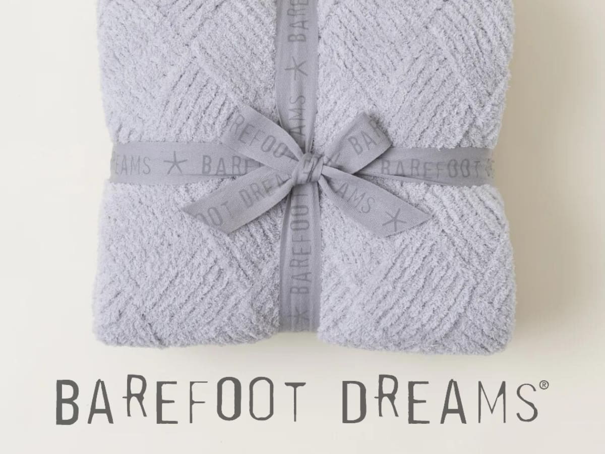 A folded light purple blanket tied with a ribbon, with the brand "barefoot dreams" displayed below.