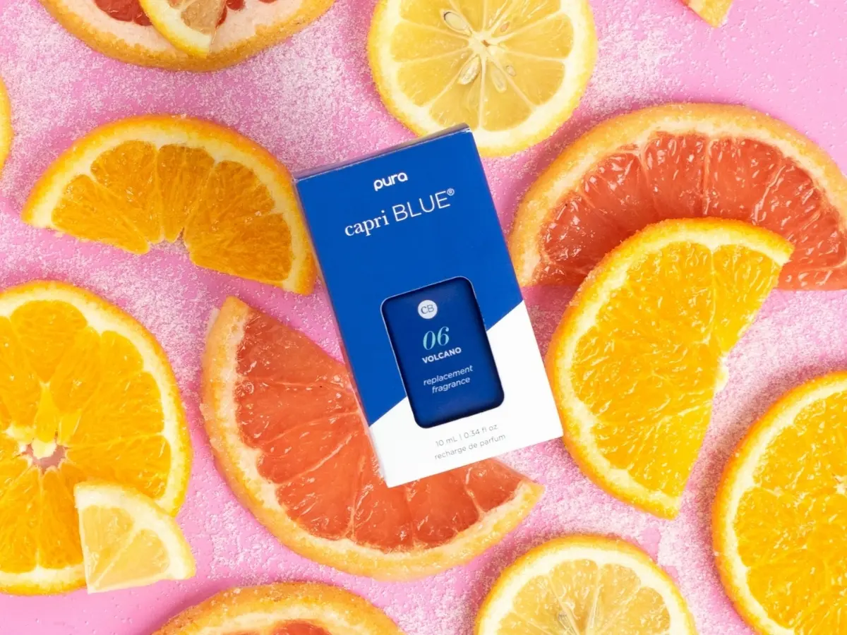 Blue fragrance packaging surrounded by sliced citrus fruits on a pink background.